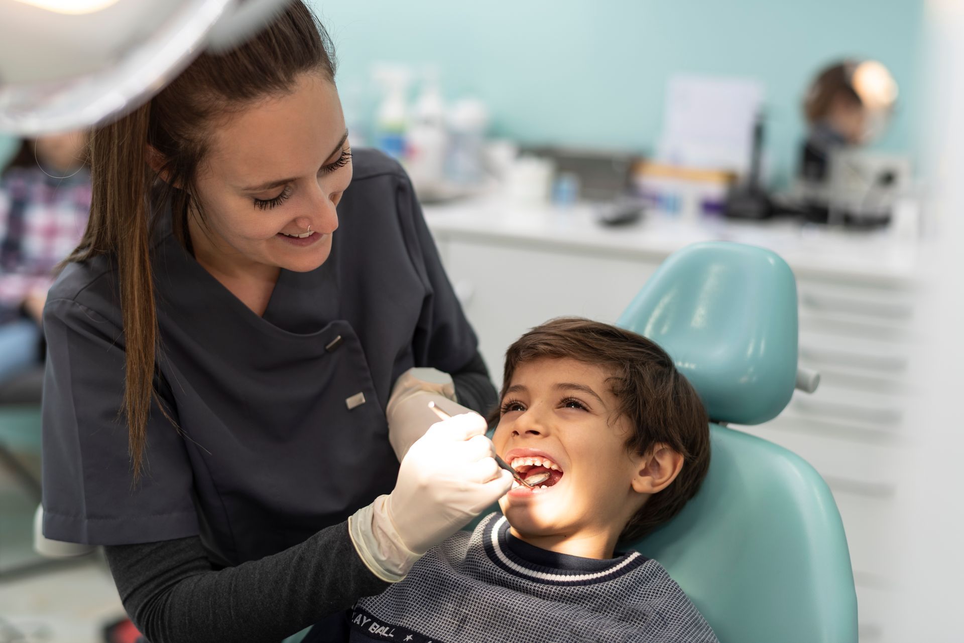 A young boy is sitting in a dental chair getting his teeth examined by a female dentist.