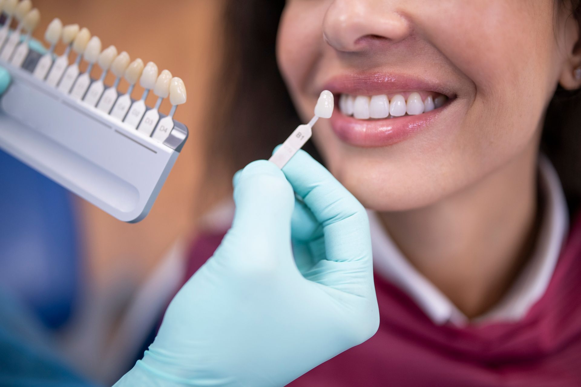 A woman with red jacket is getting her teeth whitened by a dentist.
