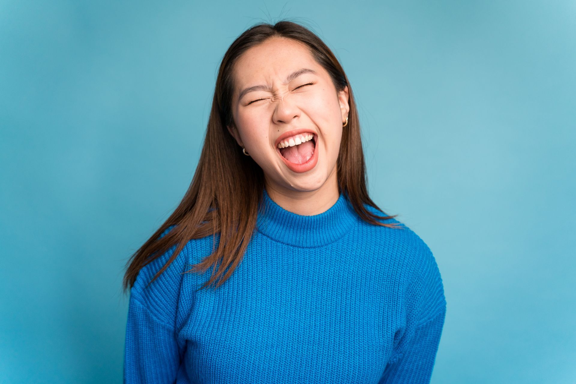 A woman in a blue sweater is laughing with her mouth open.