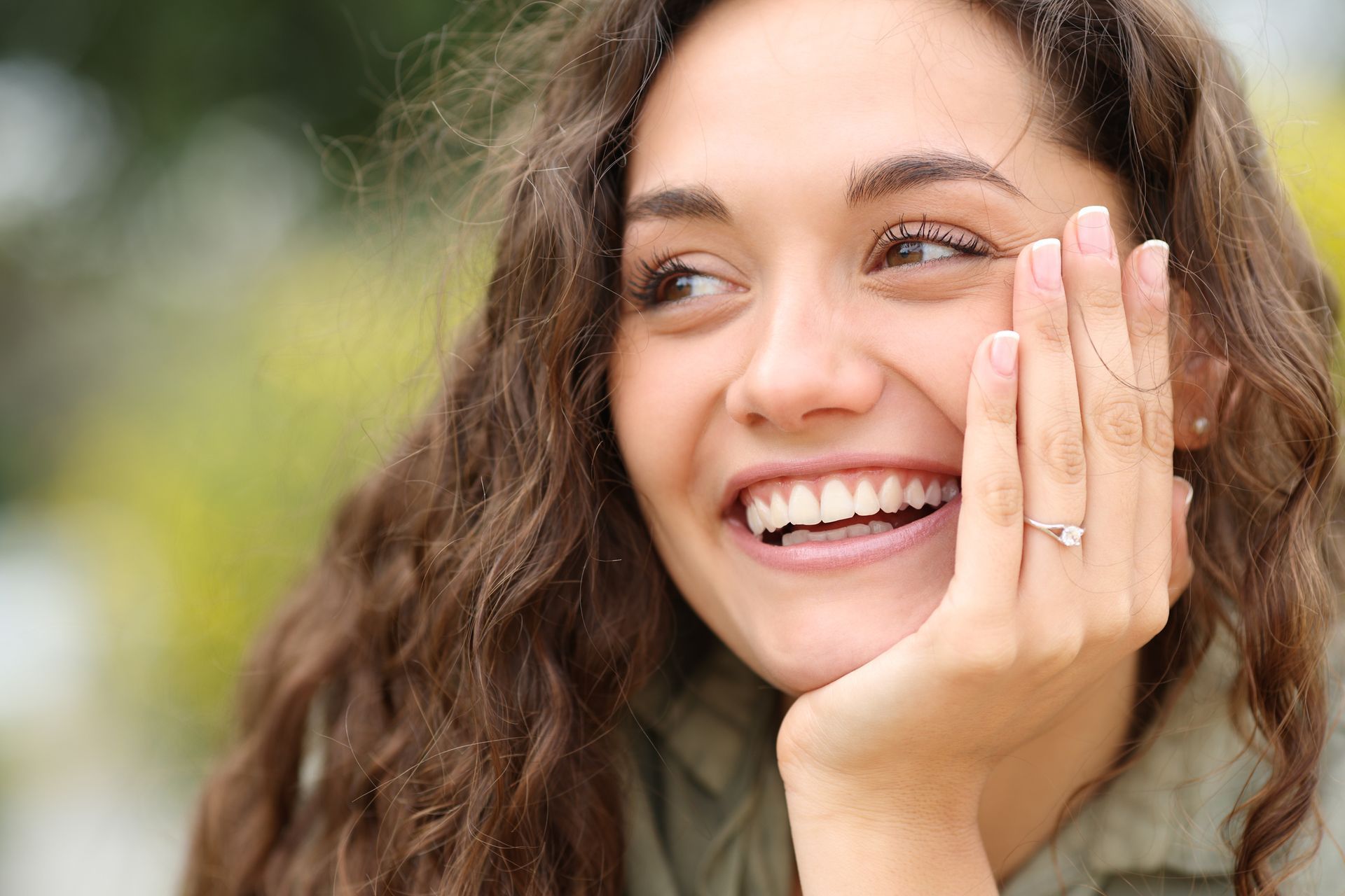 A woman with a ring on her finger is smiling and covering her face with her hand.