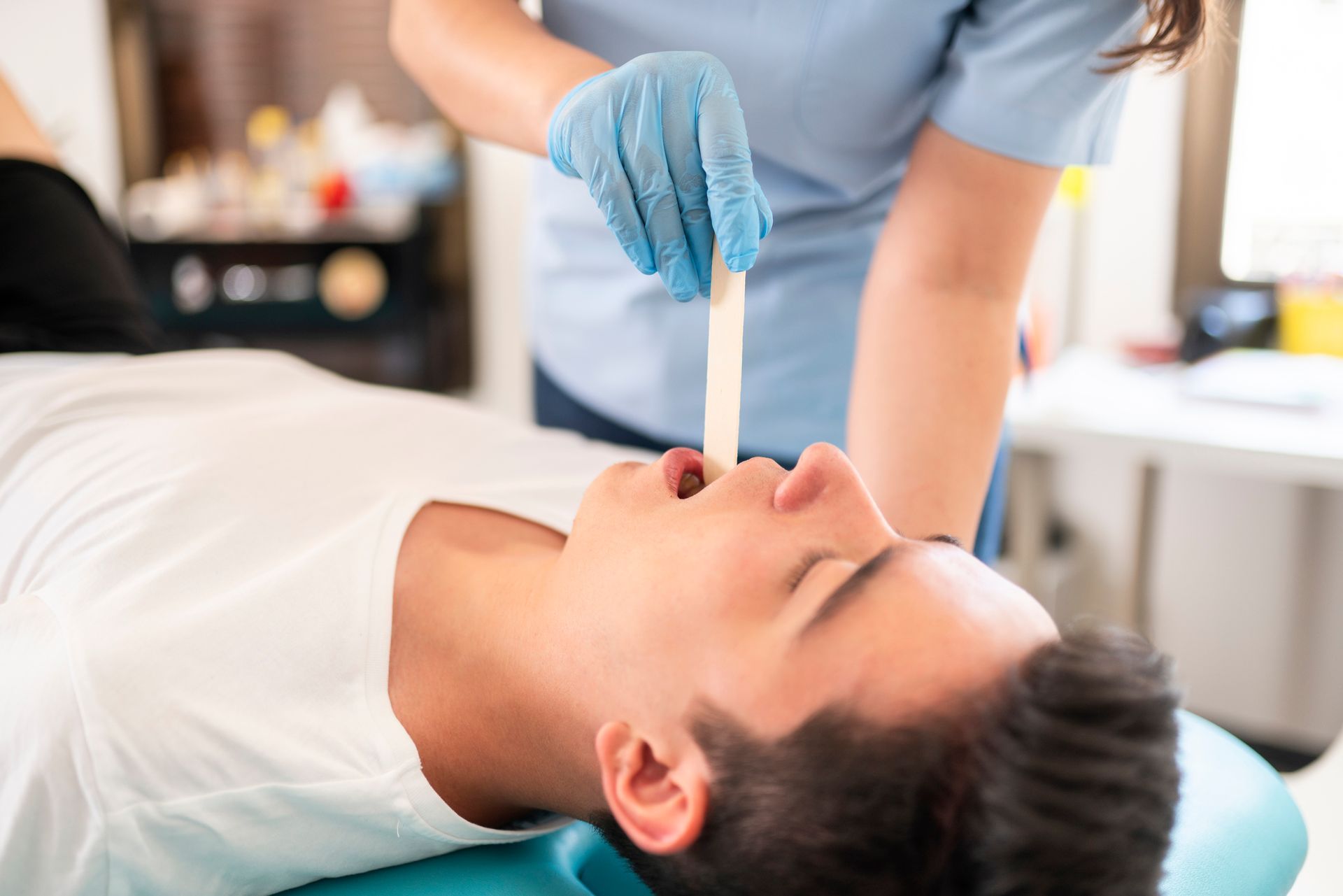 A man is laying in a dental chair while a nurse examines his tongue with a tongue depressor.