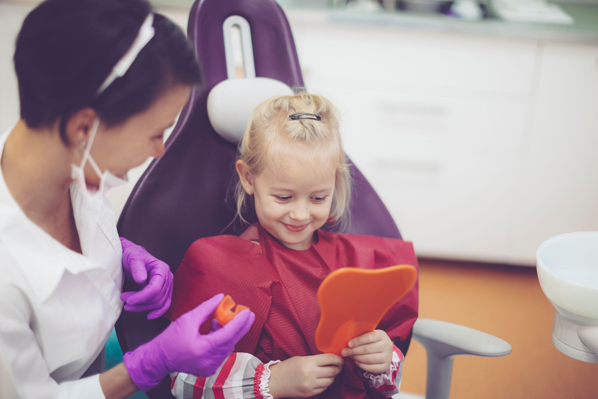 A dentist wearing pink gloves is holding a clear retainer in the shape of a heart.