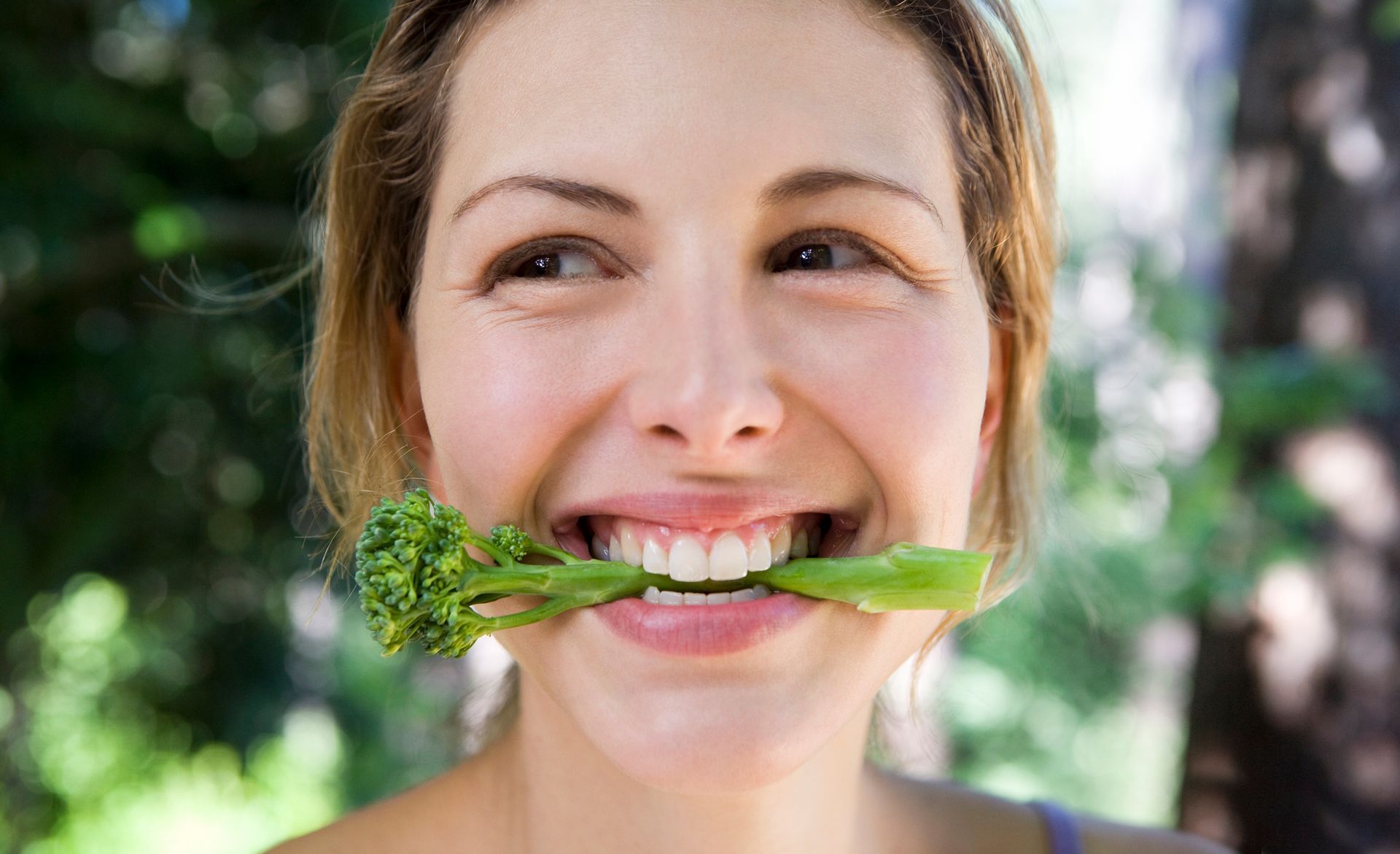 A woman is holding a piece of broccoli in her mouth.