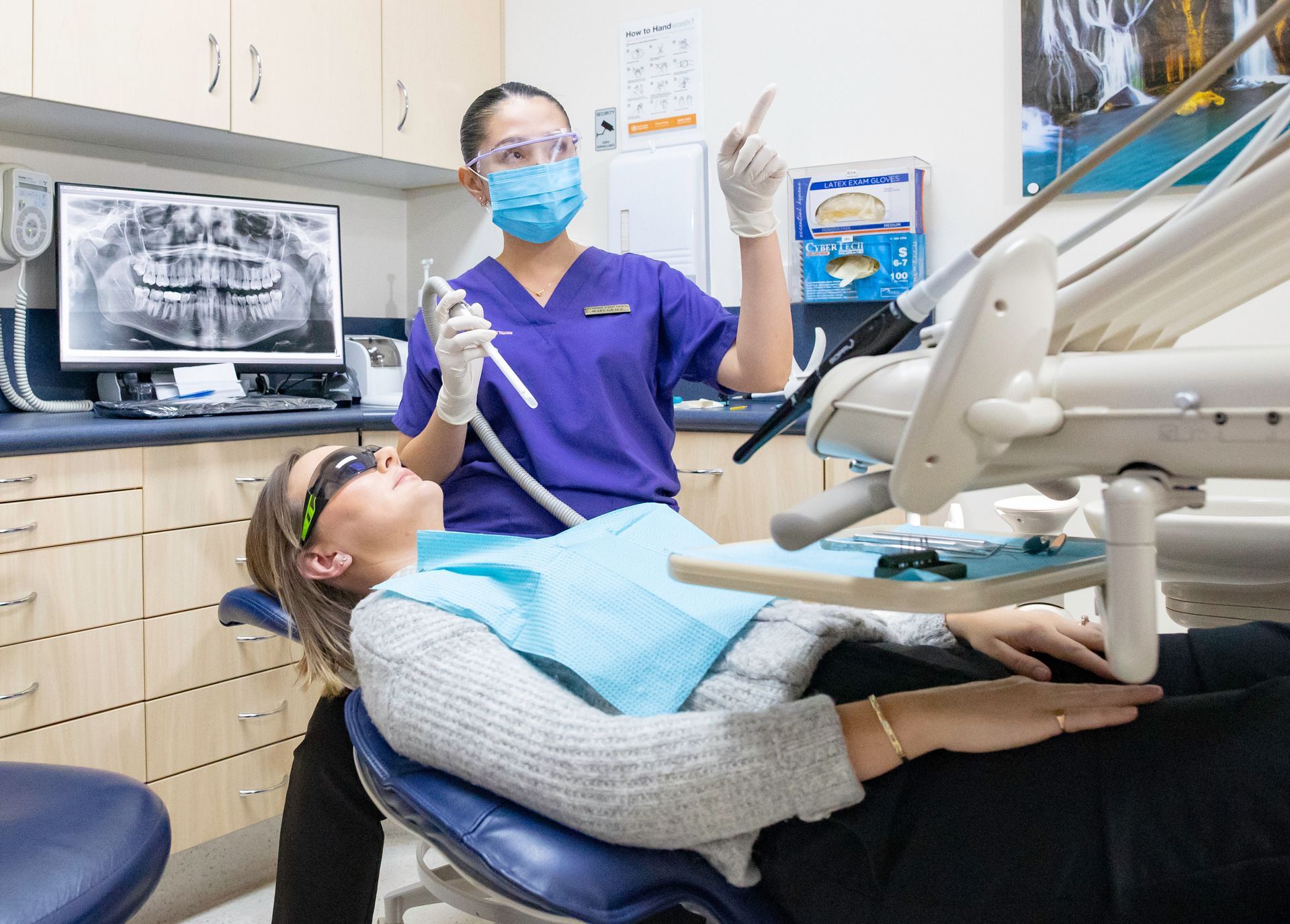 A female professional dentist is examining a patient 's teeth in a dental office.