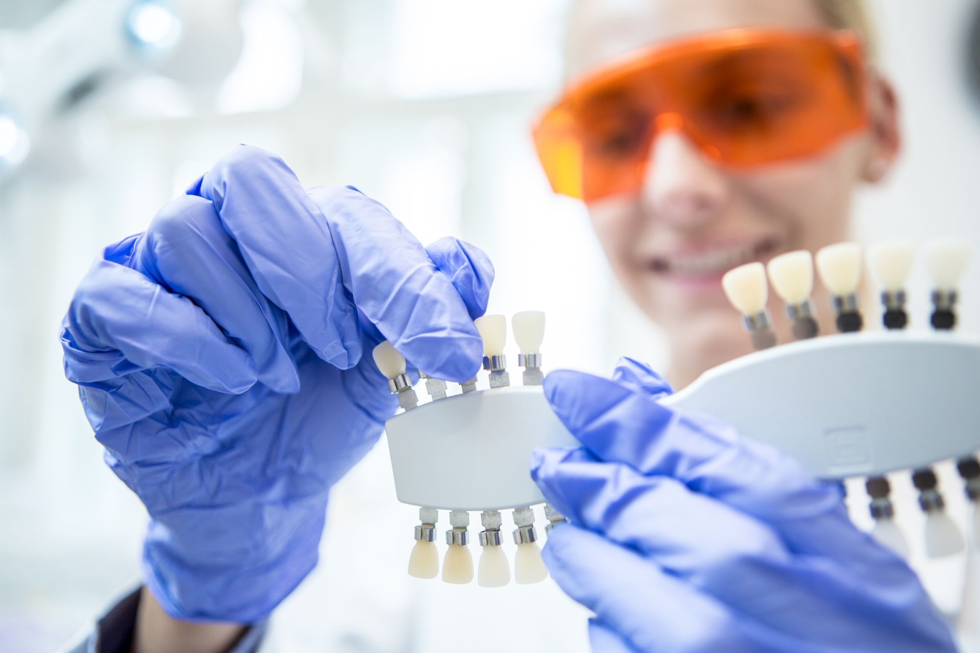 A dentist wearing gloves and sunglasses is holding a model of teeth.
