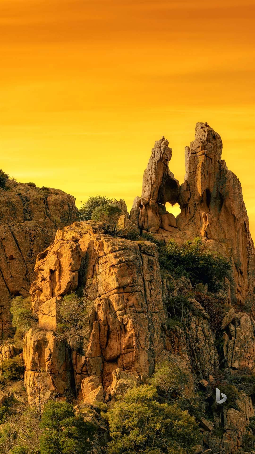 A mountain covered in rocks and trees with a sunset in the background.