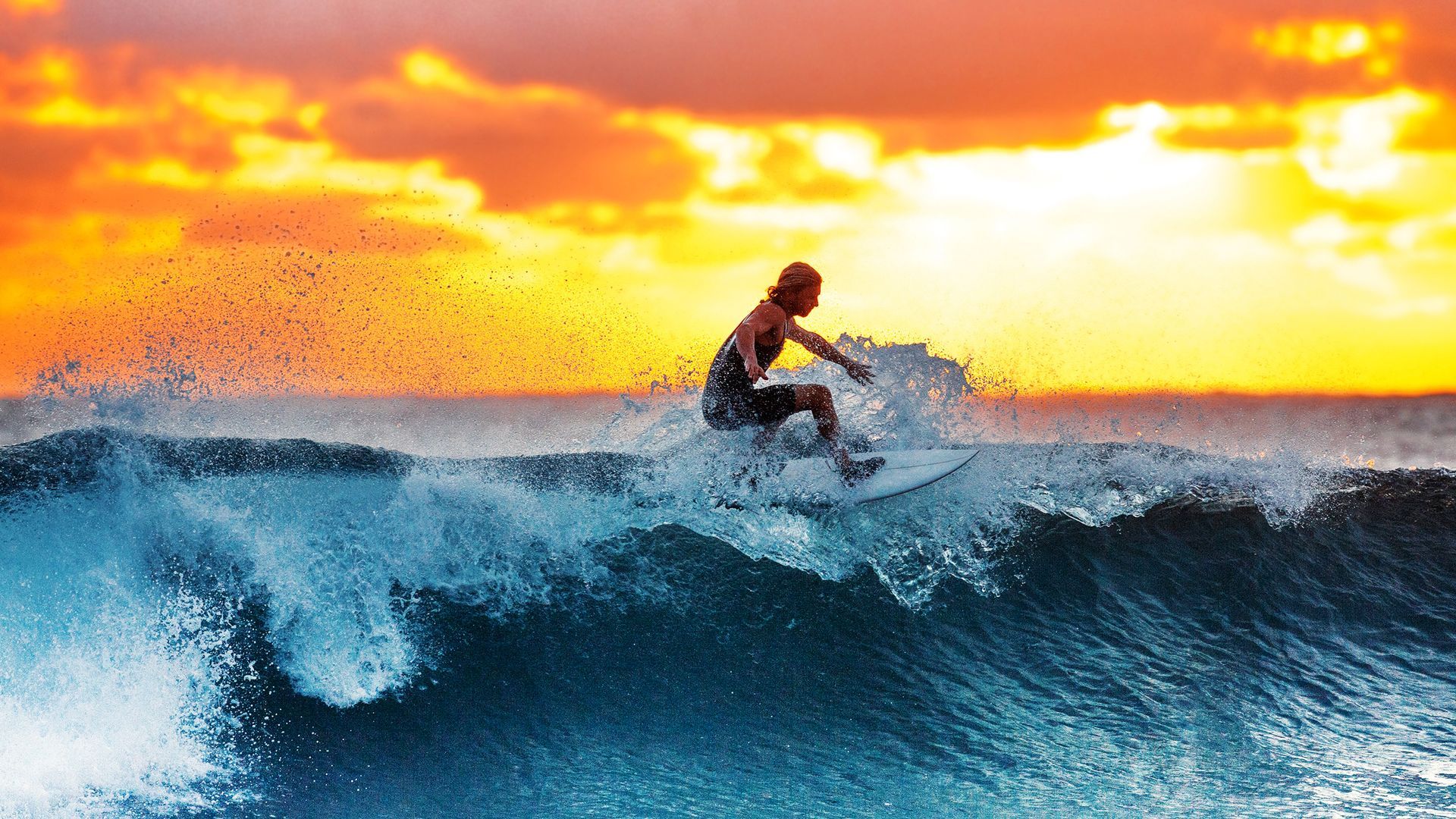 A man is riding a wave on a surfboard in the ocean at sunset.