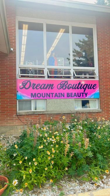 A pink and blue sign for dream boutique mountain beauty is in front of a brick building.