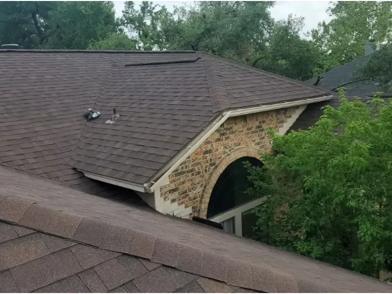 Brown shingled roof with a brick accent, trees in background.