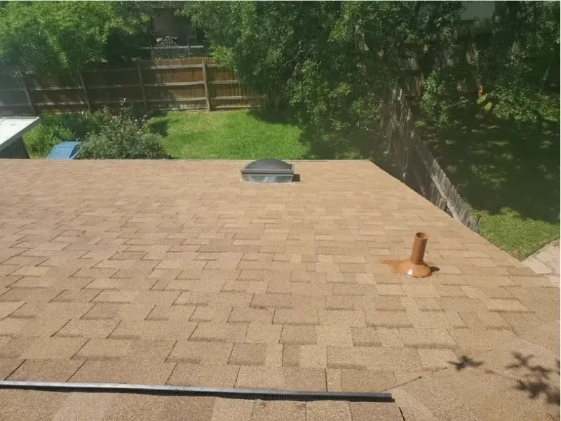 Brown shingled rooftop with a skylight, vent pipe, and surrounding backyard.