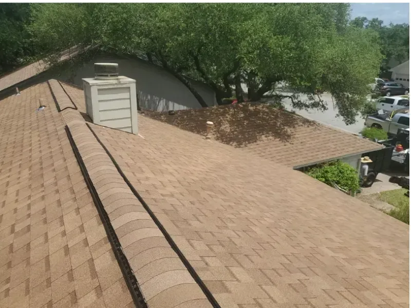 Brown shingled roof with a chimney and a large tree in the background.