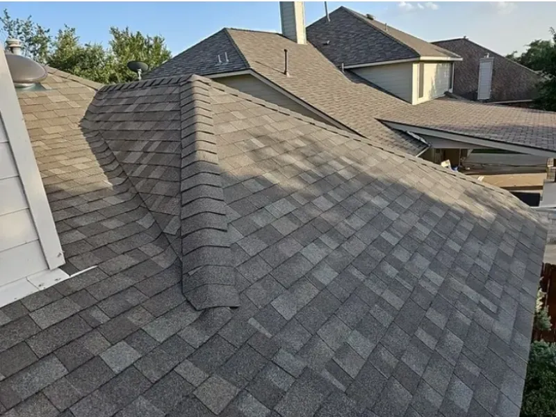 Gray and brown shingled roof with multiple angles on a house, under a clear sky.