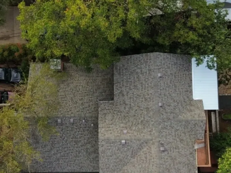 Overhead view of a house with a gray shingled roof, trees, and a mirrored side wall.