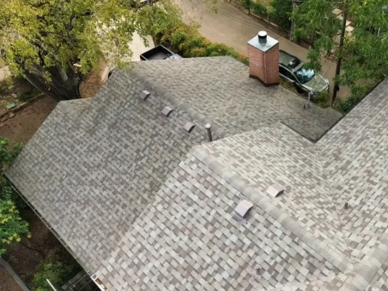 Overhead view of a house roof with asphalt shingles in shades of brown and a brick chimney.