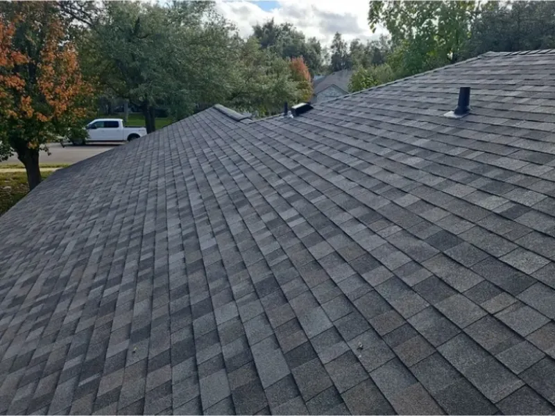 Gray asphalt shingle roof on a house, with a cloudy sky and trees in the background.