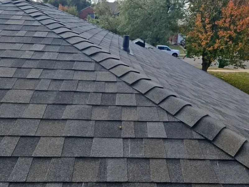 Close-up of a residential asphalt shingle roof, showing the ridge cap and a vent pipe.