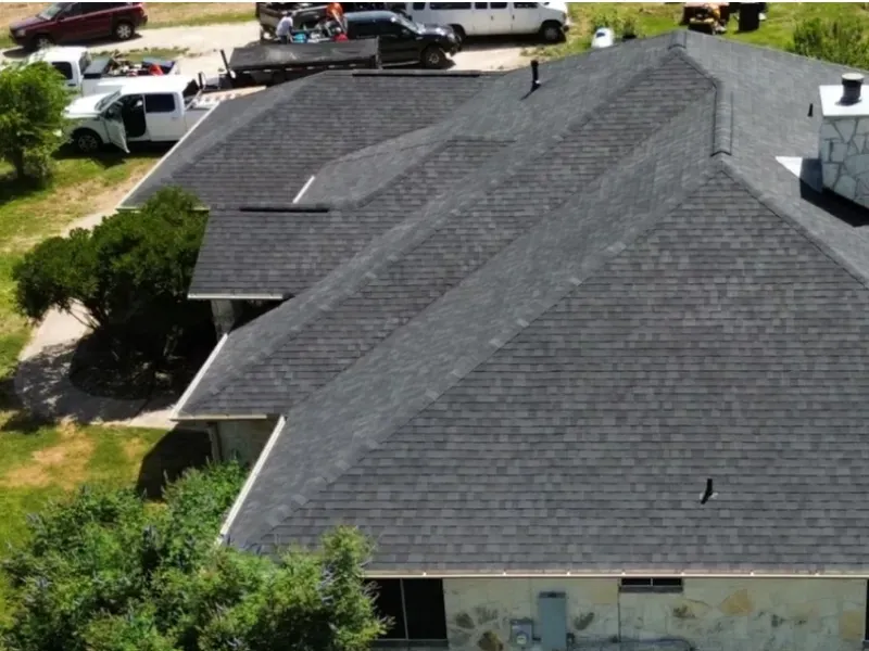 Dark gray shingled roof of a house, seen from above, with cars and people in the background.