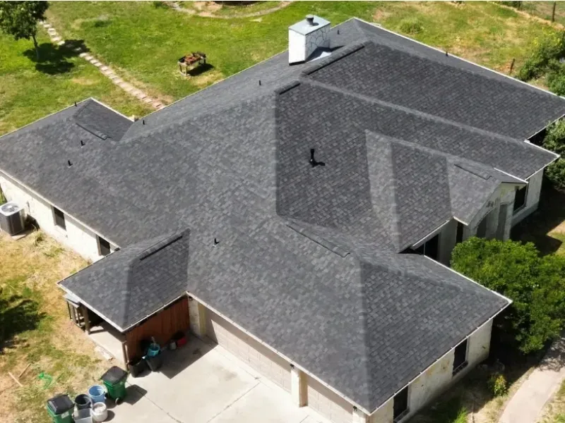 Gray shingle roof on a house with white siding and a two-car garage. Overlooking trees and grass.