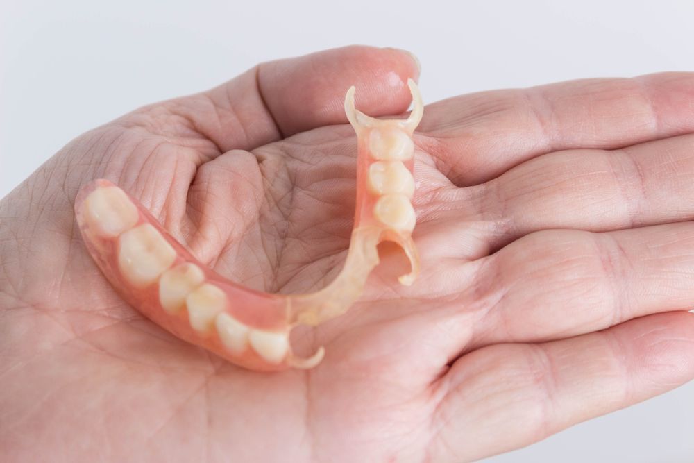 A Person is Holding a Denture in Their Hand — Dental Prosthetics By Richard & Cindy In Oxenford, QLD