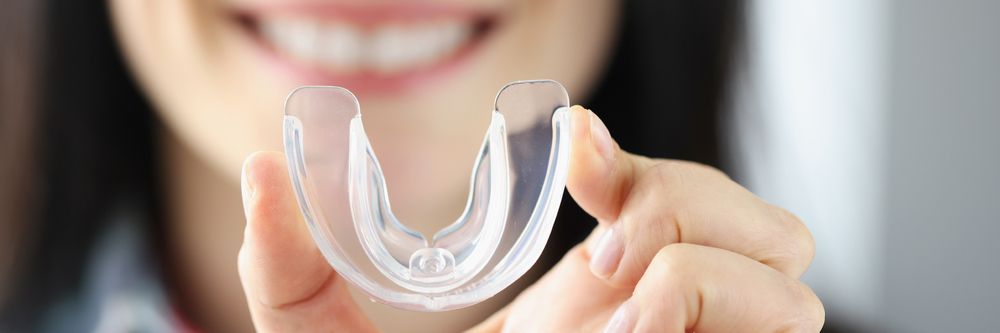 A Woman is Holding a Clear Mouth Guard in Her Hands — Dental Prosthetics By Richard & Cindy In Oxenford, QLD