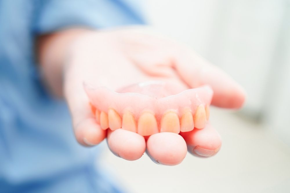 A Person is Holding a Denture in Their Hand — Dental Prosthetics By Richard & Cindy In Oxenford, QLD