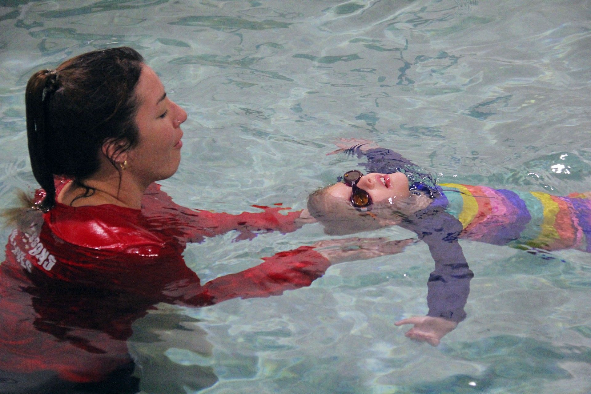Swimming lessons a woman is teaching a little girl how to swim in a swimming pool.
