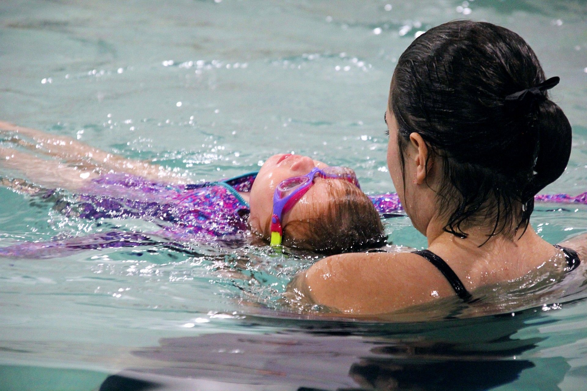 Swimming lessons a woman is teaching a little girl how to swim in a swimming pool.