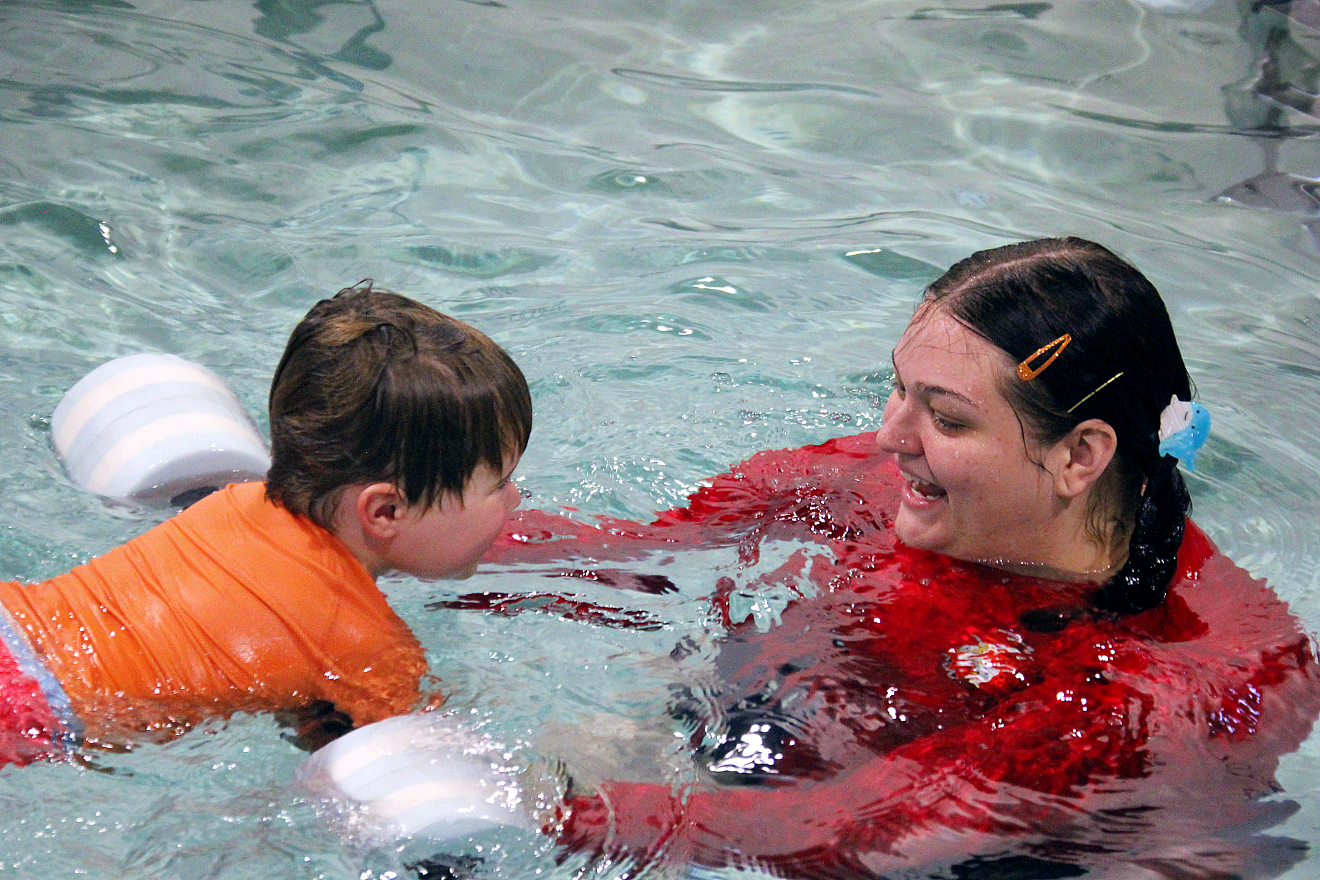 Private Swim Lessons a woman is teaching a child how to swim in a swimming pool.