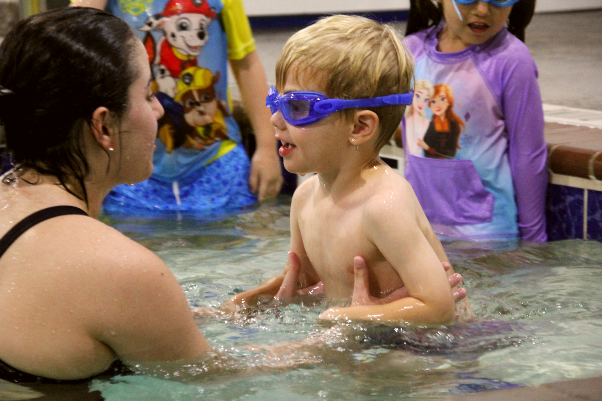 Swimming lessons a woman is teaching a young boy how to swim in a pool.