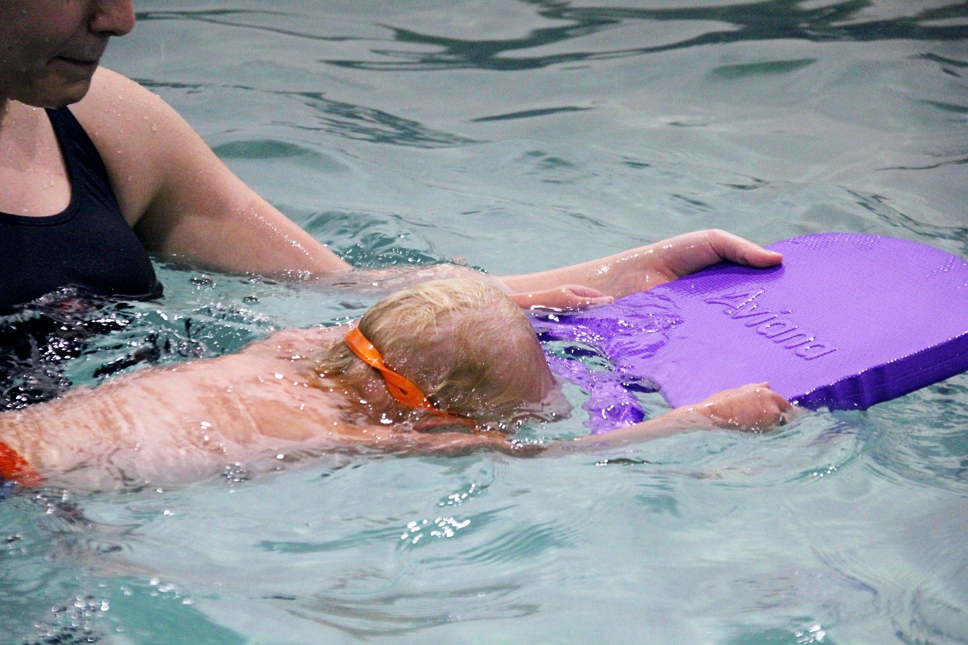 A woman is swimming in a pool wearing a yellow swim cap and goggles.