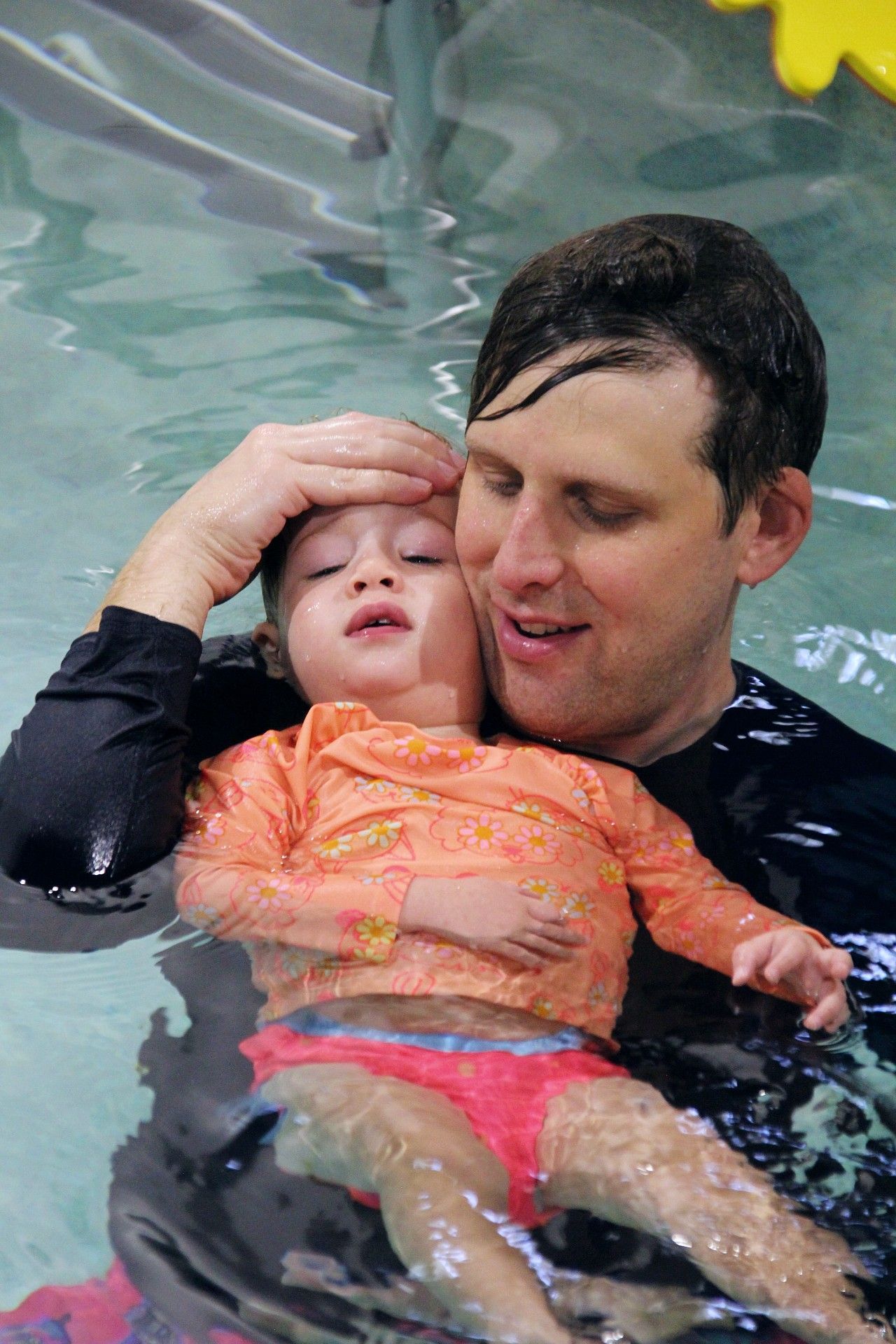 Swimming lessons a baby is swimming in a pool and smiling at the camera.
