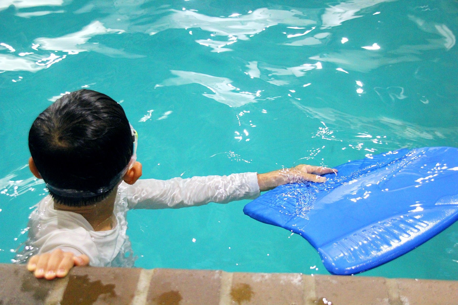 A child is holding a blue board in a swimming pool