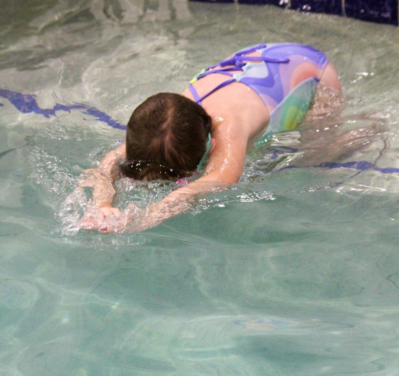 A young girl in a purple swimsuit is swimming in a pool