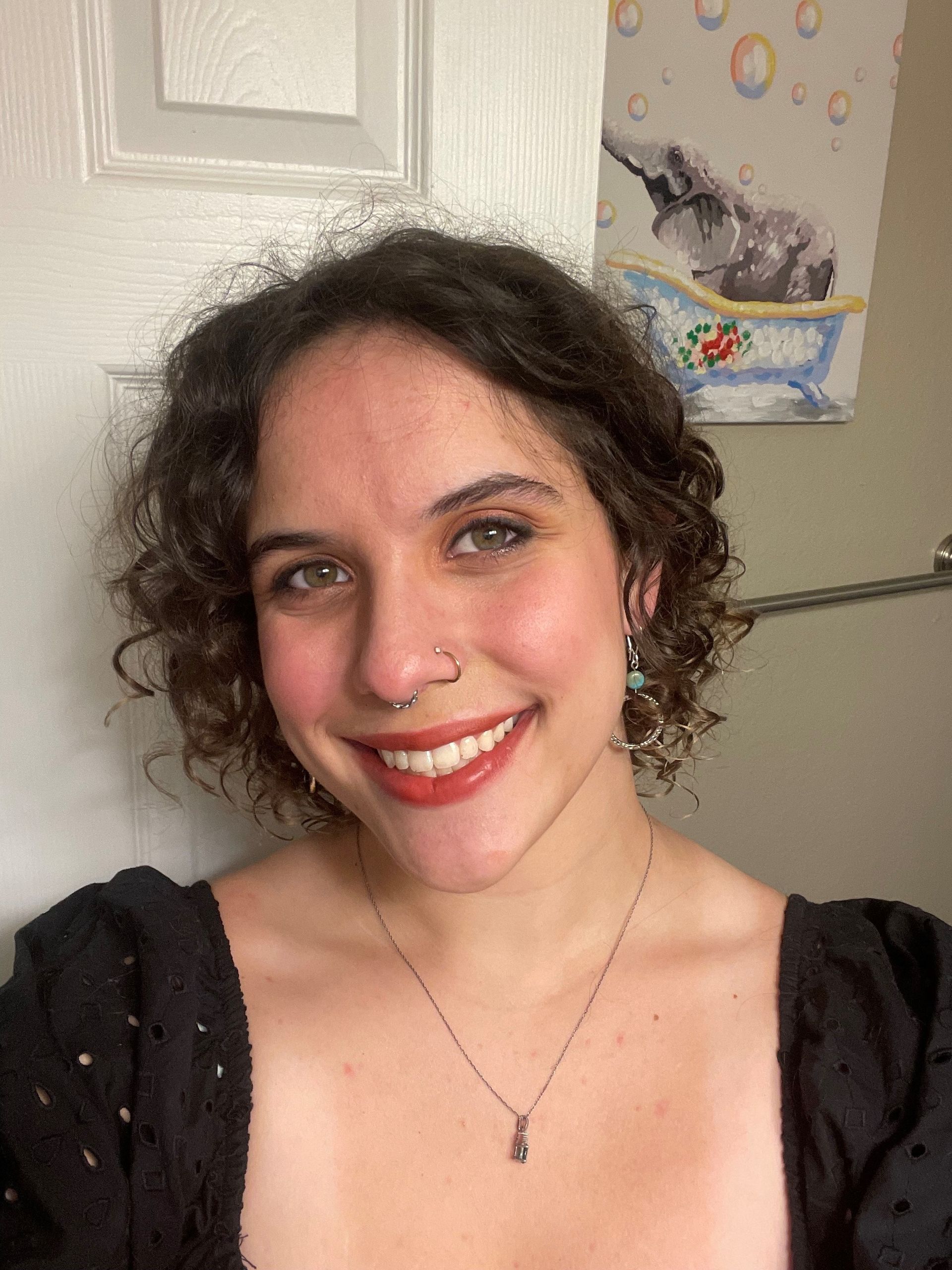 A woman with curly hair and a nose ring is smiling for the camera.