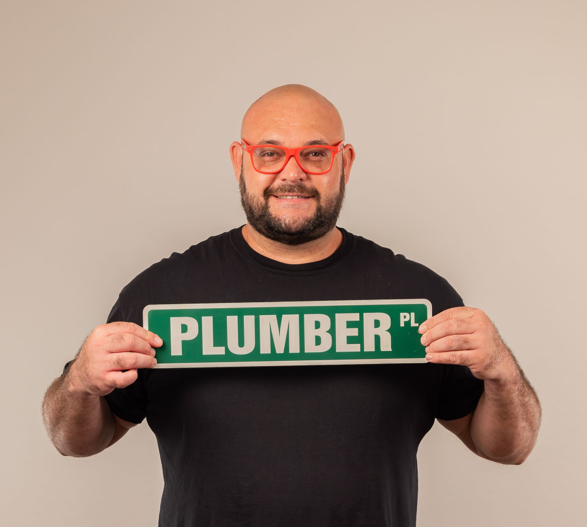A man wearing glasses is holding a sign that says plumber