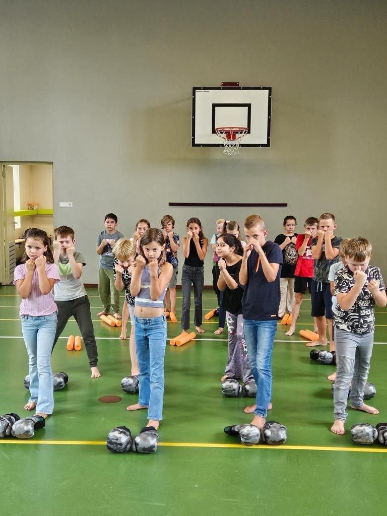 Kinderen in een gymzaal doen boksoefeningen. Ze staan ​​met hun handen omhoog, vlak bij hun gezicht.