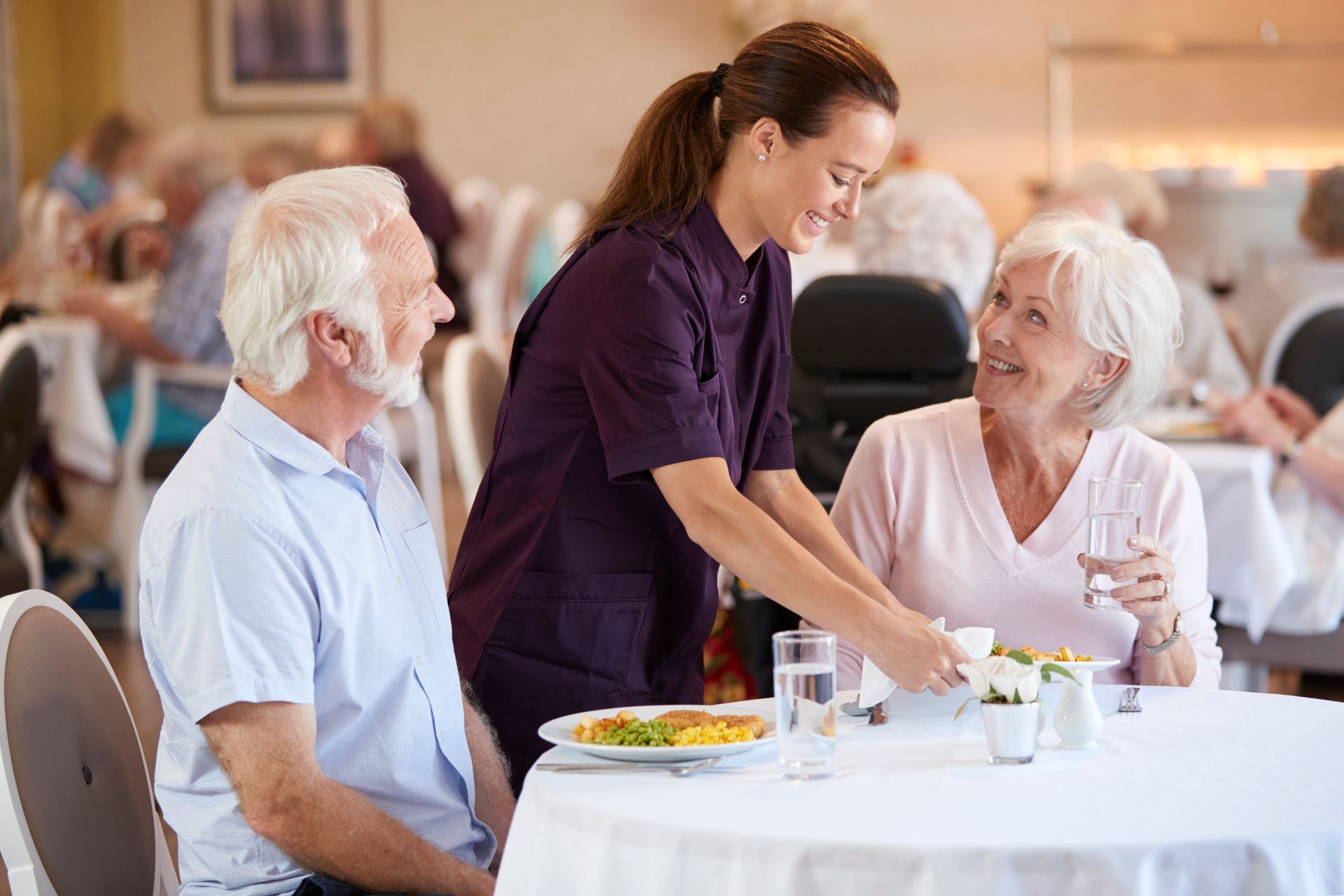 A nurse is serving food to two elderly people in a restaurant.