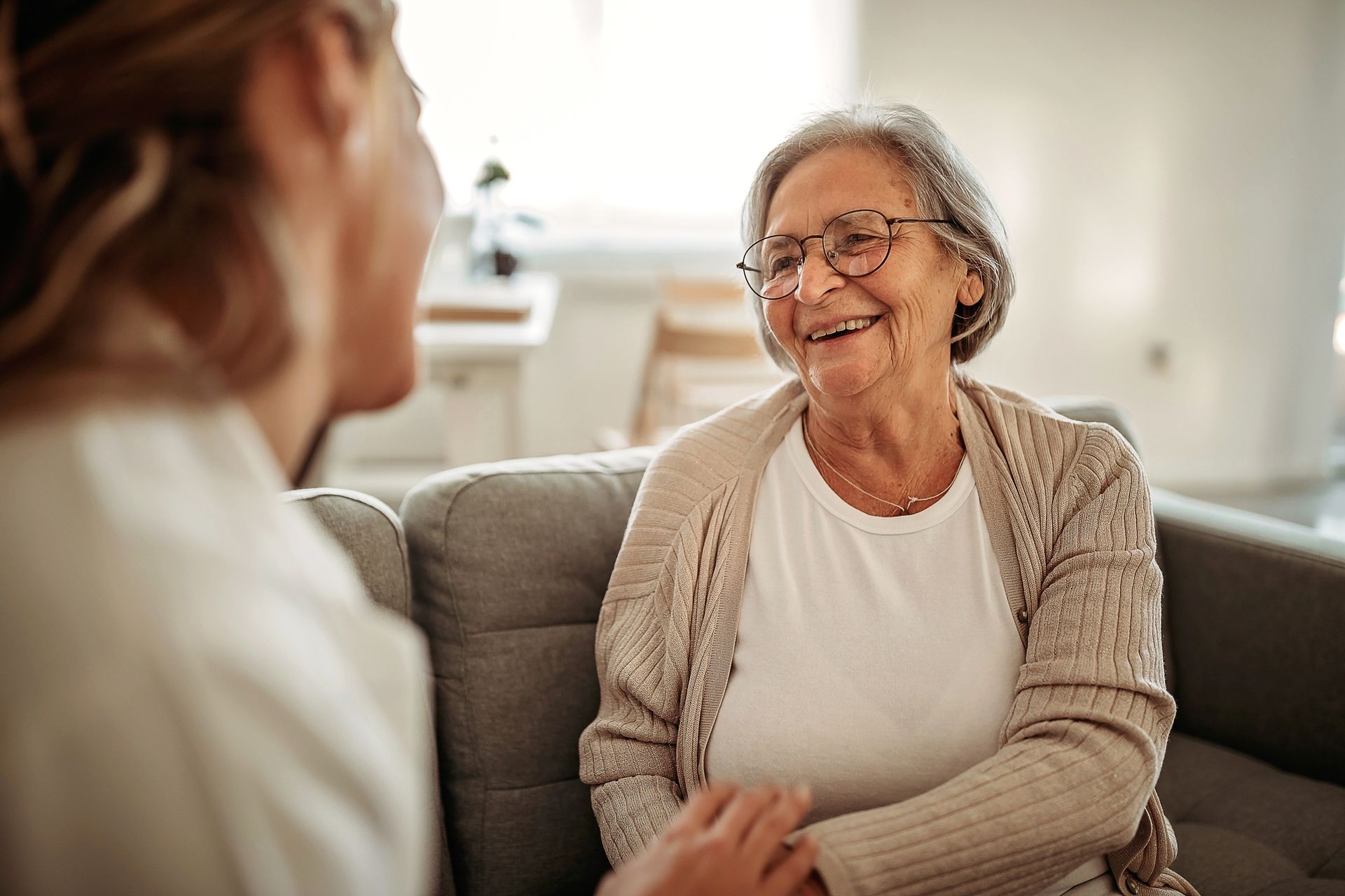 An elderly woman is sitting on a couch talking to a nurse.