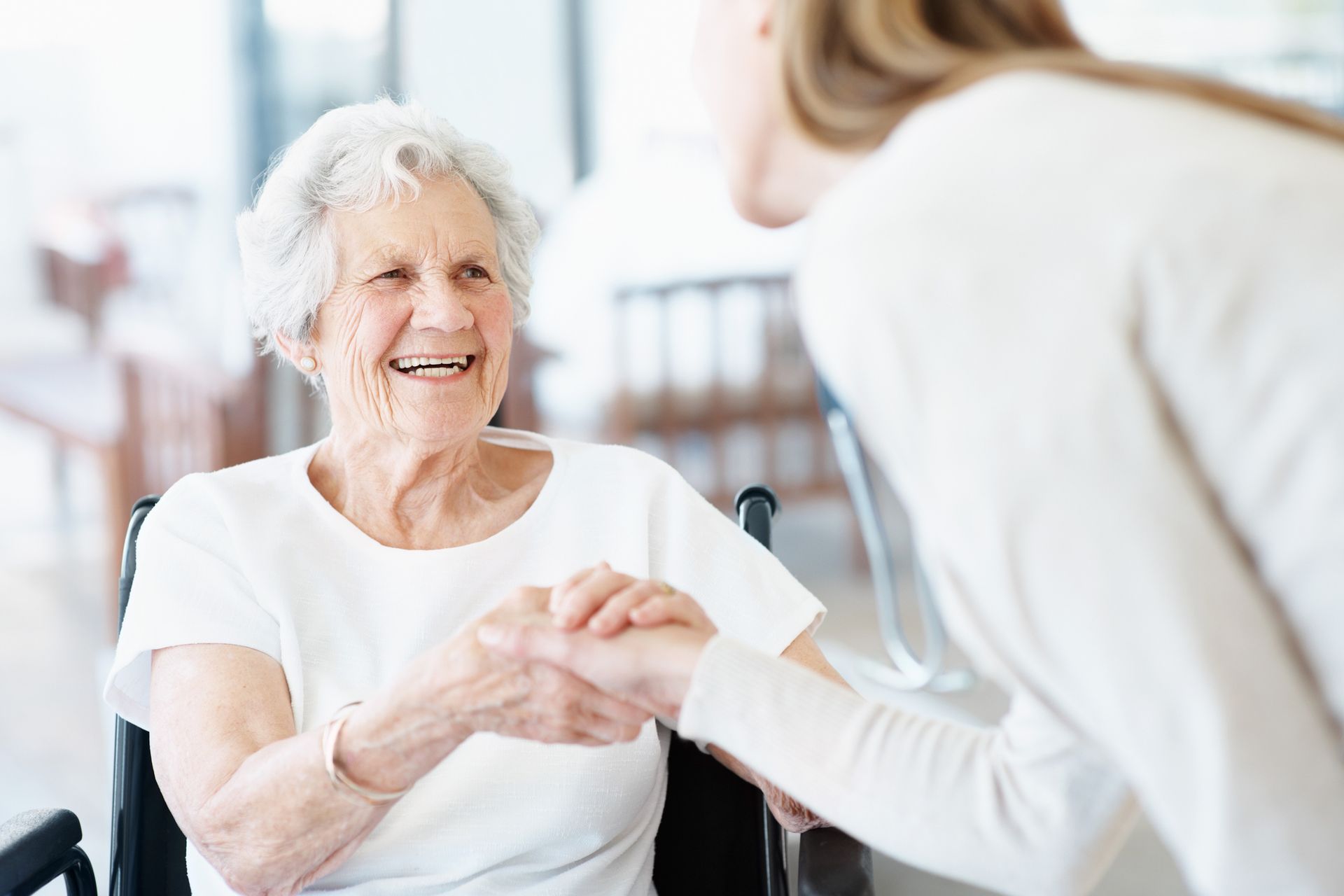 A woman is holding the hand of an elderly woman in a wheelchair.