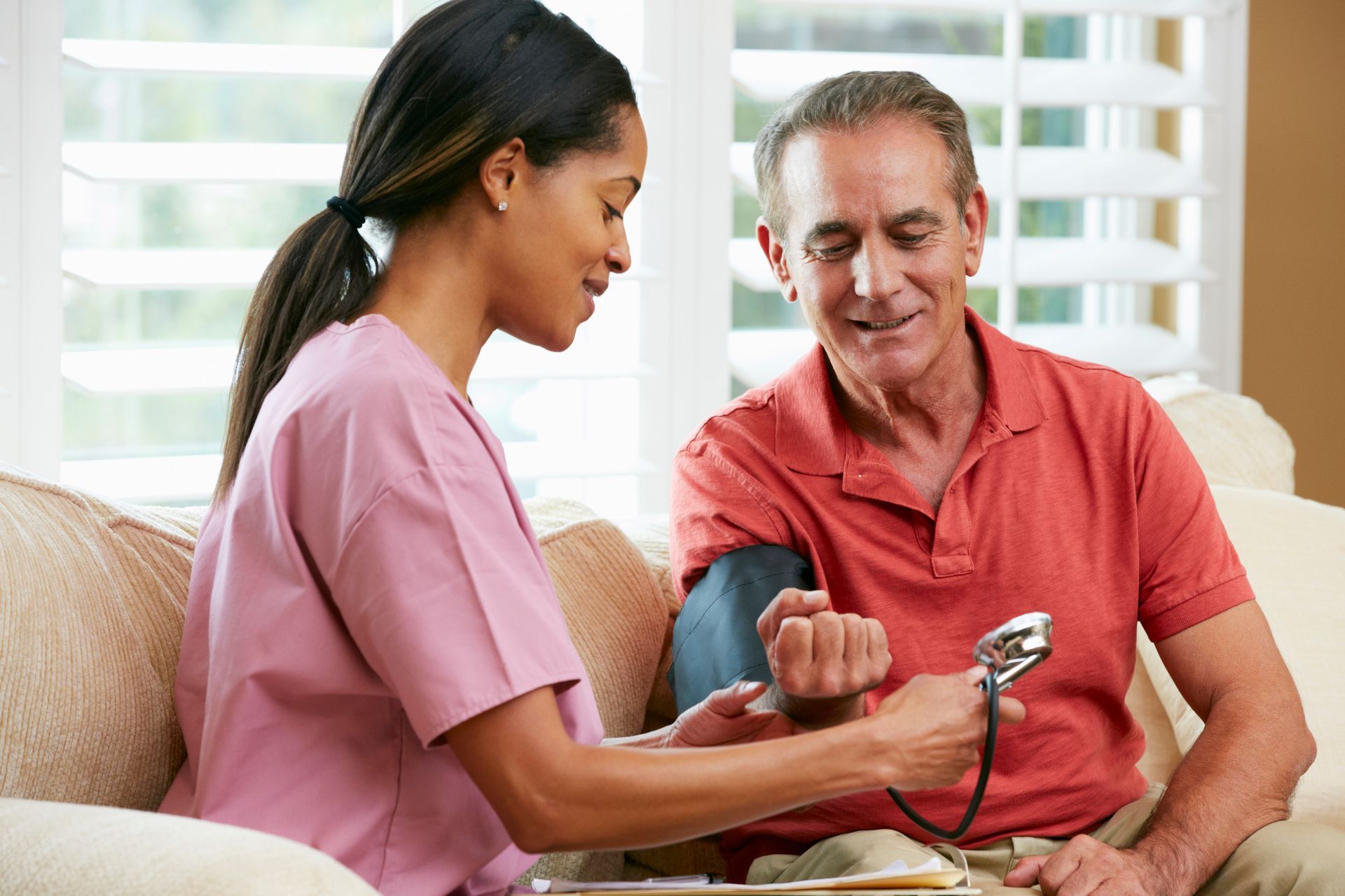 A healthcare worker in pink scrubs measures an elderly man's blood pressure.