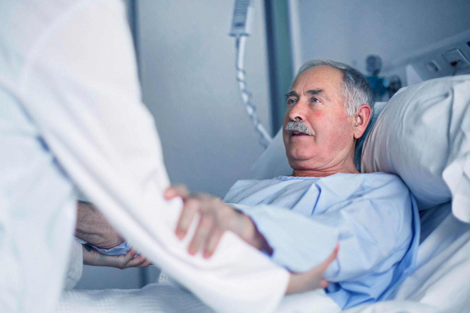 An elderly man is laying in a hospital bed holding a nurse 's hand.