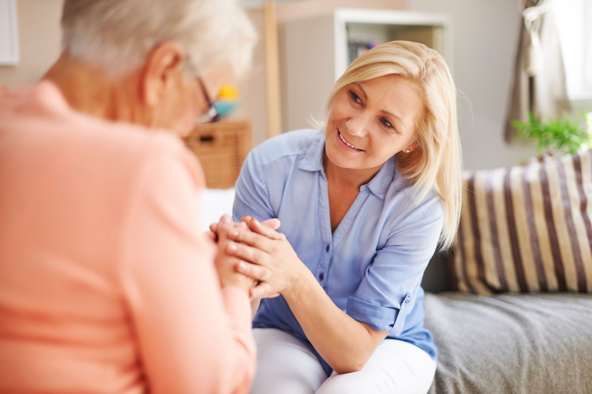 A woman is holding the hand of an older woman while sitting on a couch.