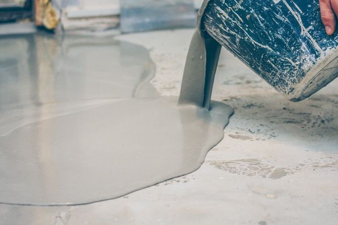 A person is pouring concrete into a hole in the floor.