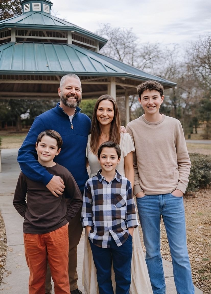 Family of five poses in front of a gazebo: two boys, a teen, and their parents. Cloudy day.