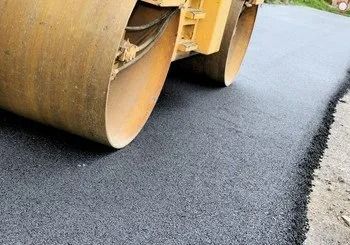Residential building with freshly sealed asphalt driveway; orange cone near sewer.