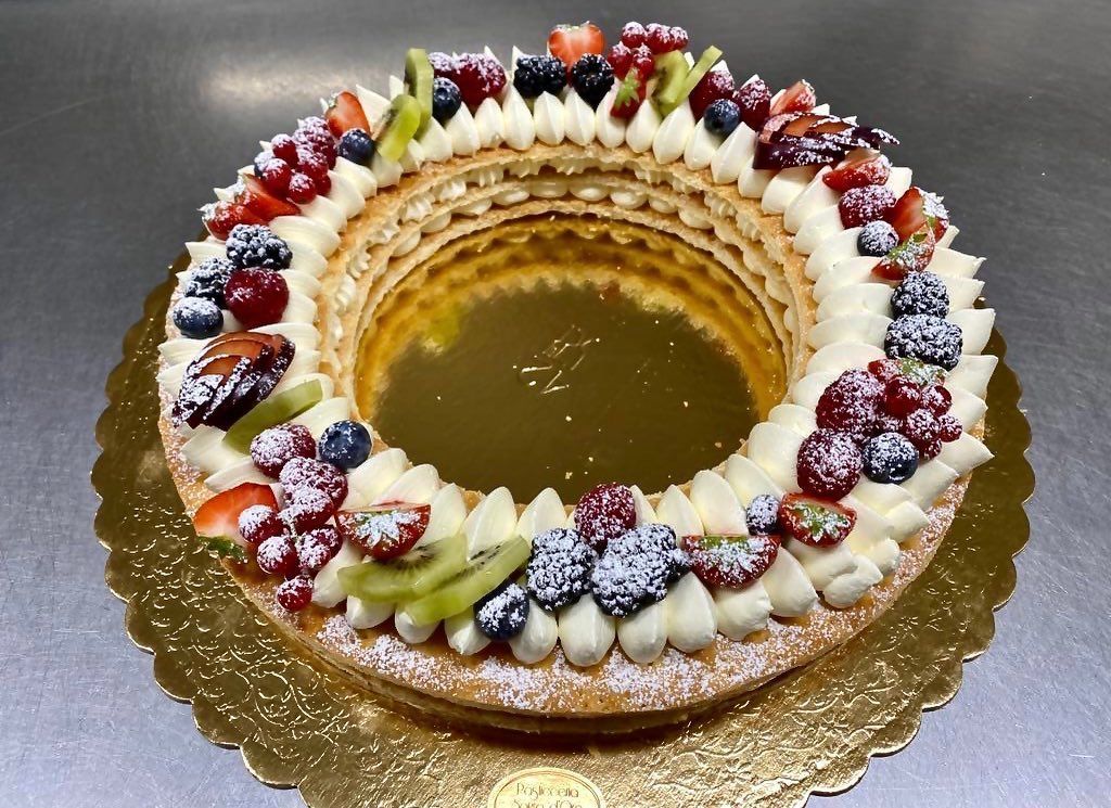 Pasta sfoglia a forma di anello con glassa alla crema e frutti di bosco misti su un tagliere dorato