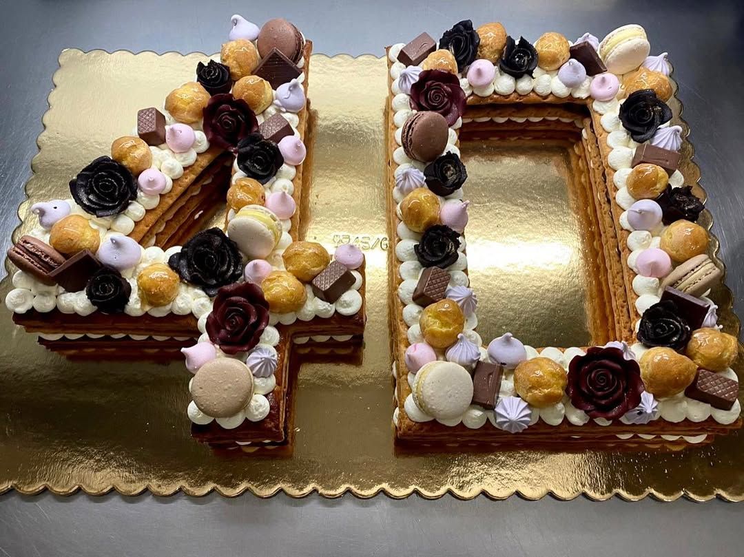 Torta a forma di numero 40, decorata con panna, cioccolatini, macaron e fiori, su una tavola dorata.