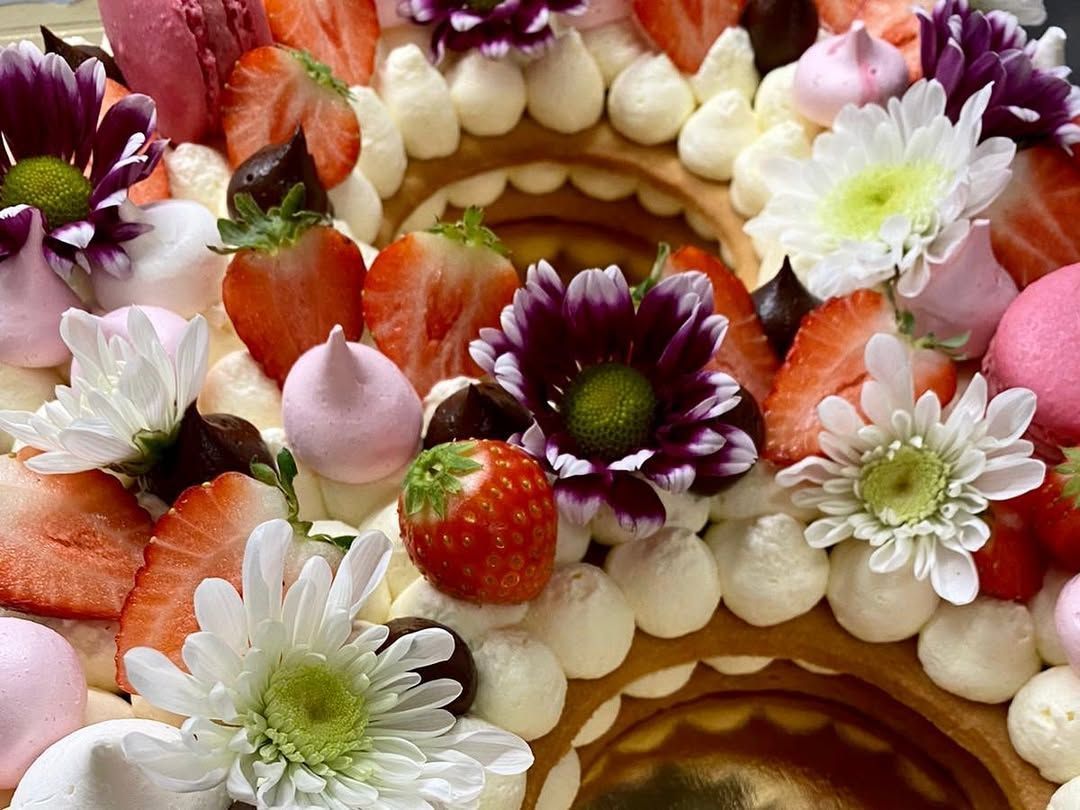 Primo piano di una torta a strati decorata con fragole, fiori, panna e macaron.