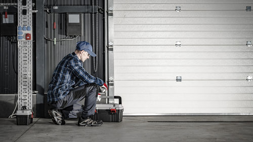 A man is kneeling down in front of a garage door.