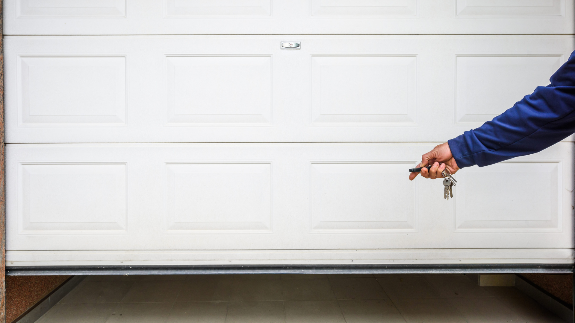 A person is holding a pair of keys in front of a garage door.